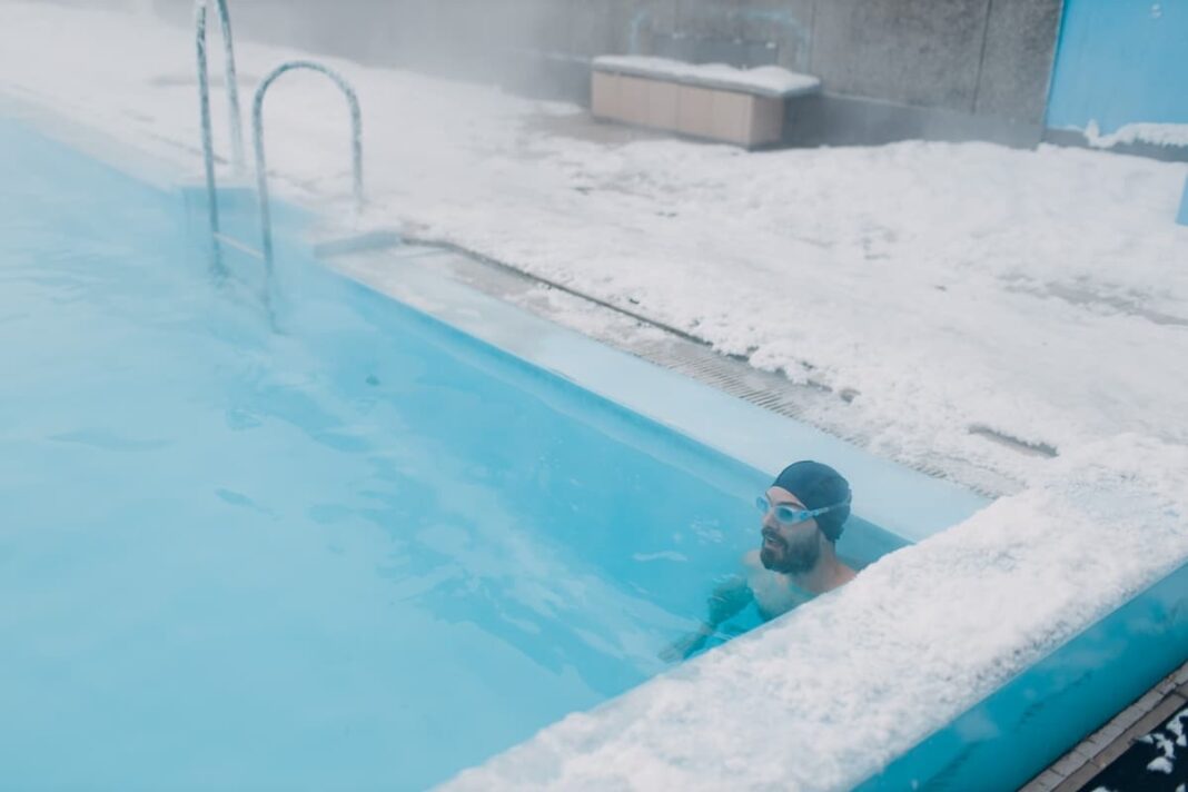 Winter open swimming pool. Swimmer man swims in steam outdoor
